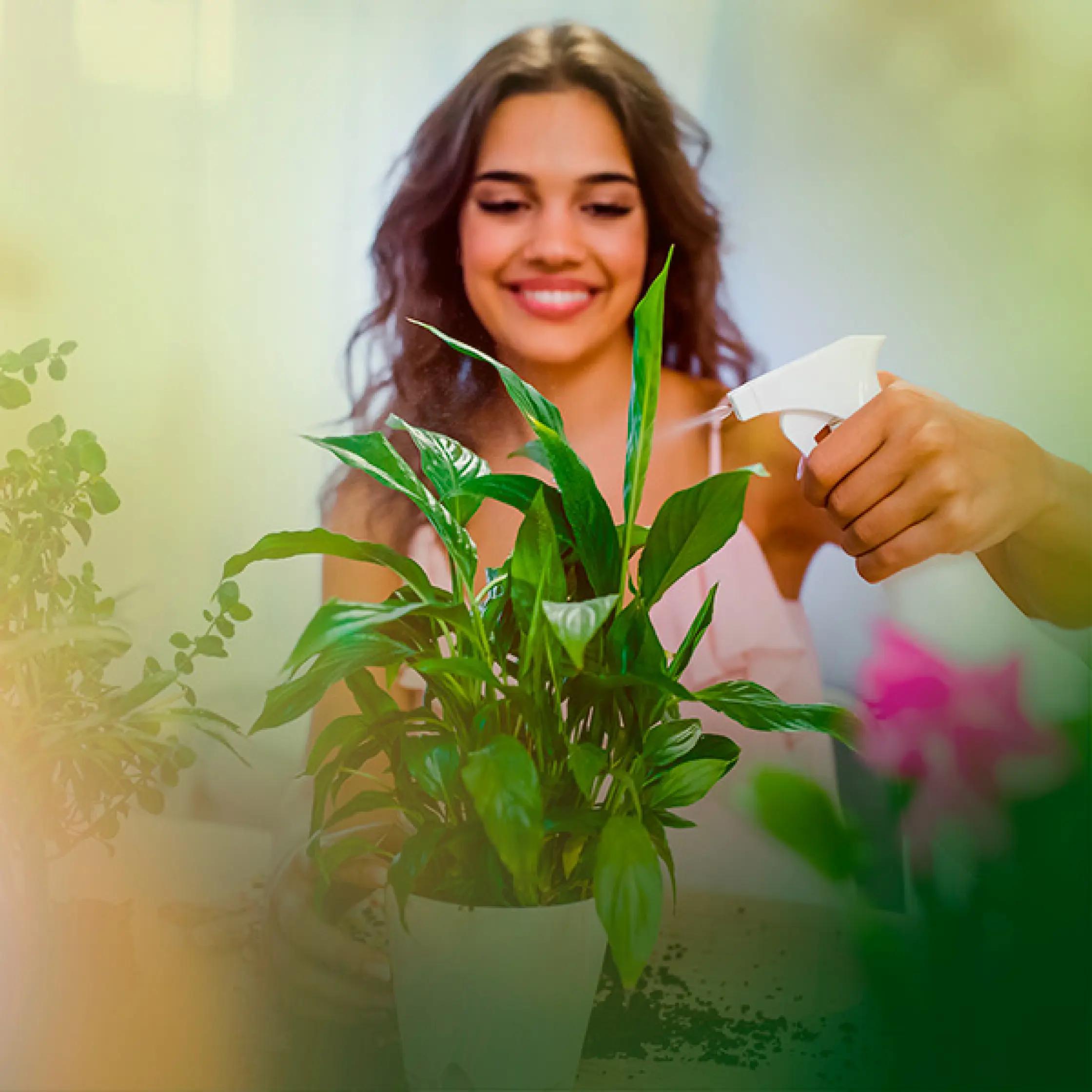 Uma mulher sorrindo regando uma planta com um borrifador